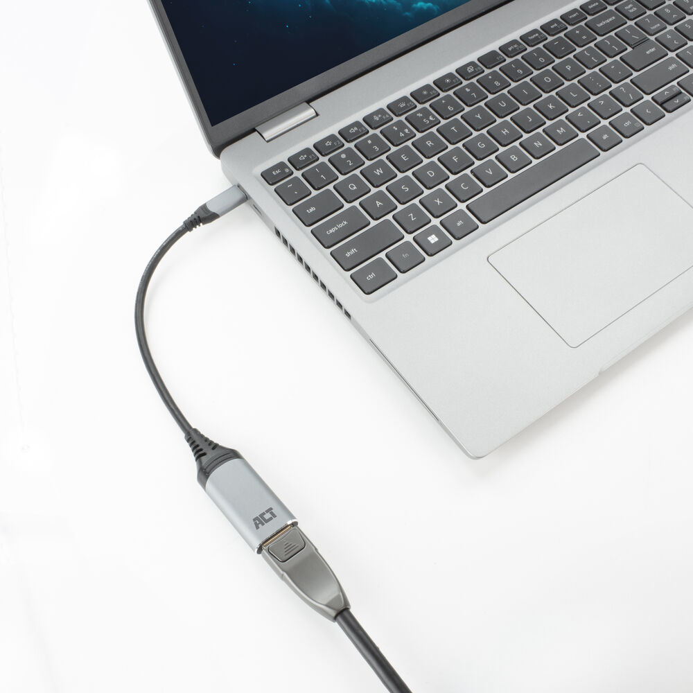 Un laptop collegato a un adattatore ACT tramite un cavo. Il laptop è aperto, mostrando la tastiera. Lo sfondo è bianco.