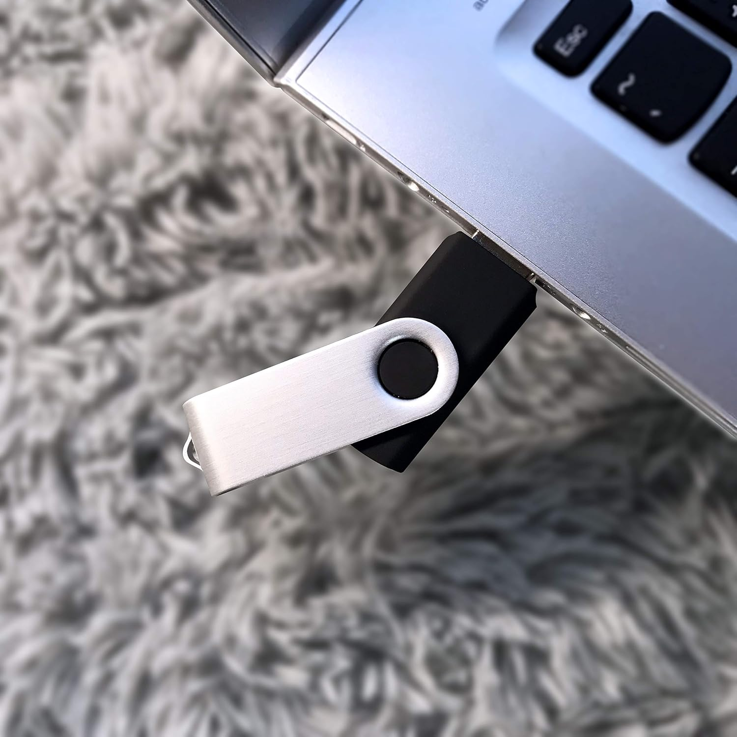Ein silberner USB-Stick ist an einen Laptop angeschlossen. Der Hintergrund ist eine verschwommene graue Oberfläche.