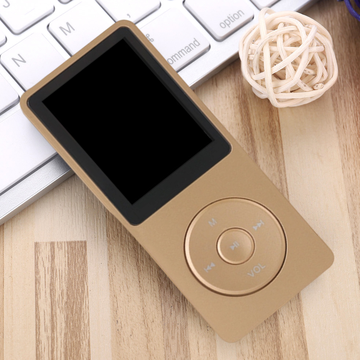 Ein goldfarbener MP3-Player mit schwarzem Bildschirm liegt auf einer Holzoberfläche neben einer weißen Tastatur und einem geflochtenen Ball.