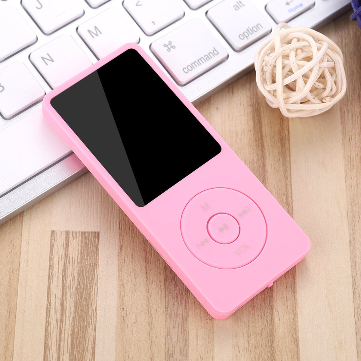 Ein pinkfarbener MP3-Player mit schwarzem Bildschirm liegt auf einer Holzoberfläche neben einer Tastatur und einem Deko-Ball.