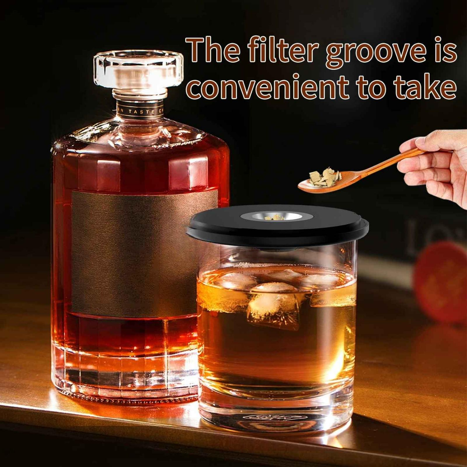 Eine Flasche und ein Glas mit bernsteinfarbener Flüssigkeit und Eis, ein schwarzer Deckel, ein Holzlöffel mit Holzspänen und eine Hand.