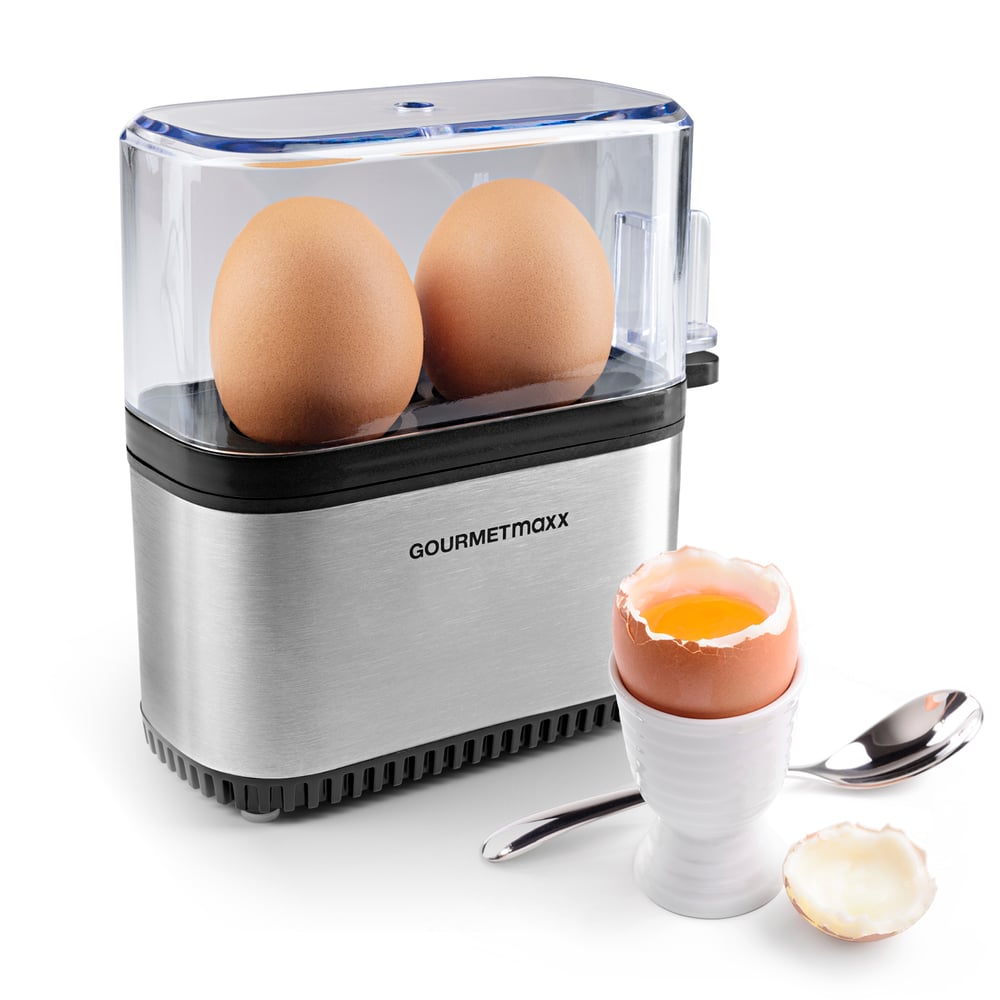 Urządzenie do gotowania jajek z dwoma jajkami w środku i jajkiem na miękko w kieliszku, łyżeczką i skorupkami.