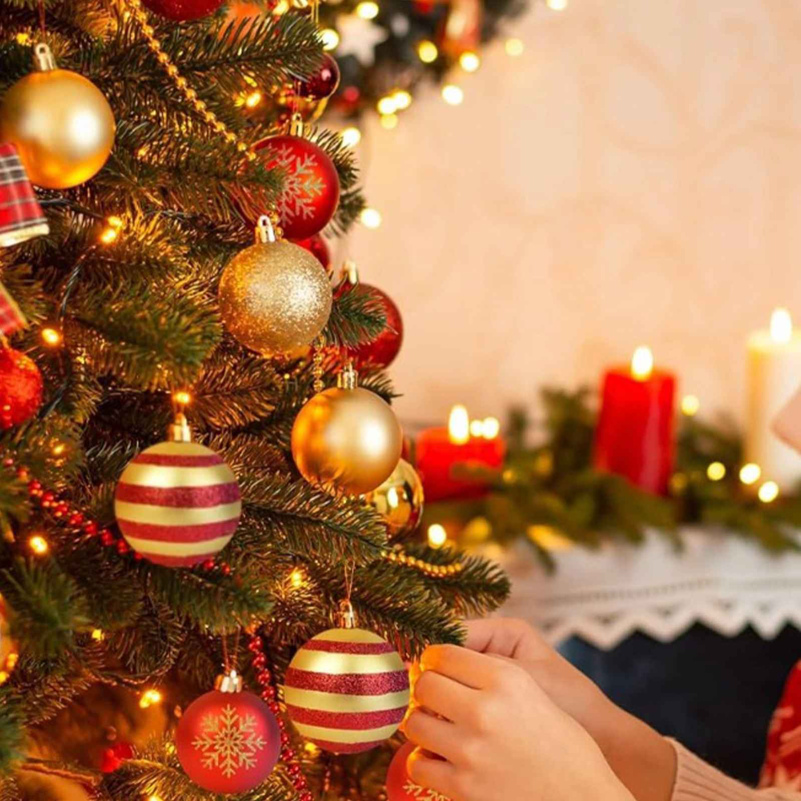 Weihnachtsbaum mit Ornamenten, Lichtern und Kerzen. Hände schmücken den Baum.