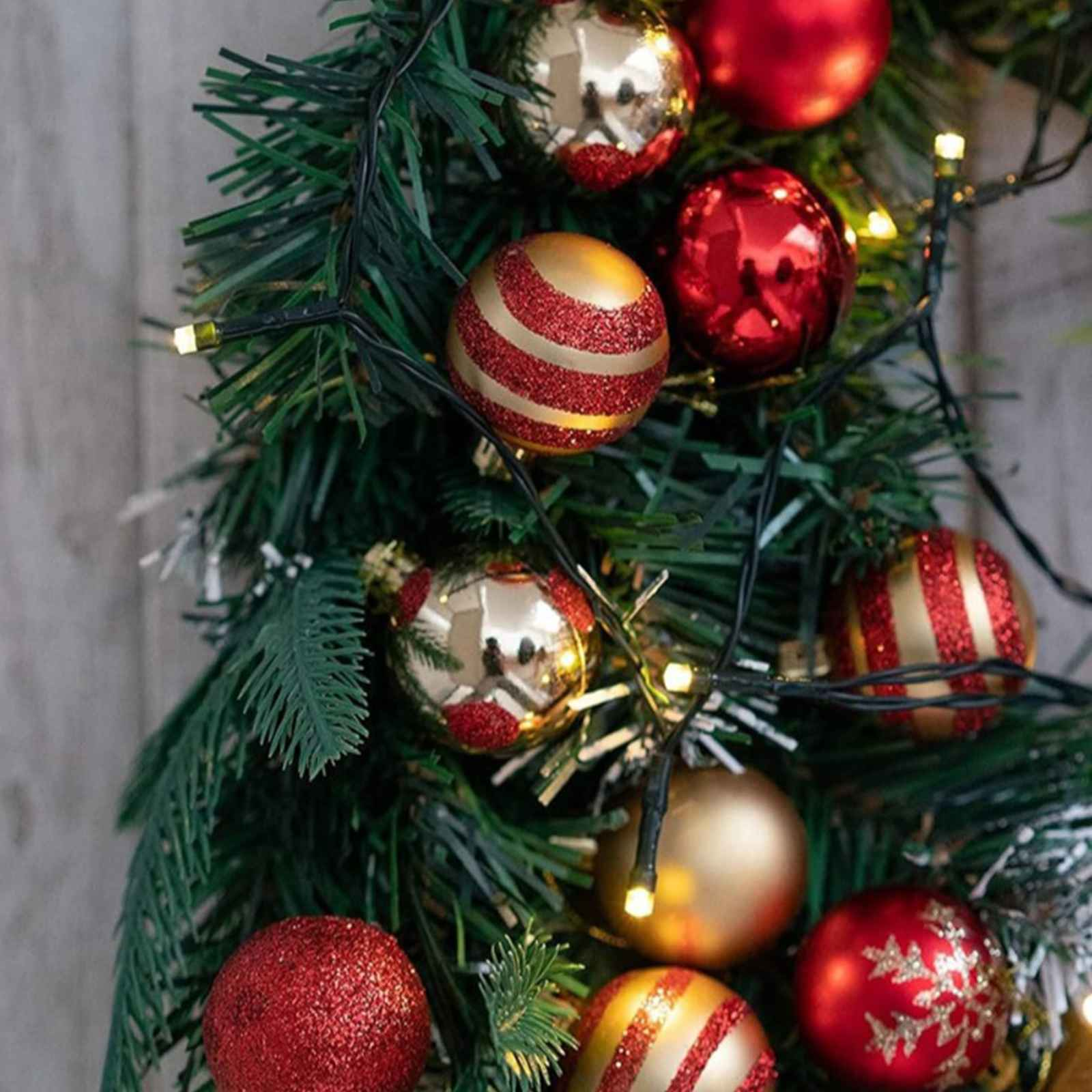 Nahaufnahme eines Weihnachtsbaums mit roten und goldenen Ornamenten und Lichtern vor einem Holzuntergrund.