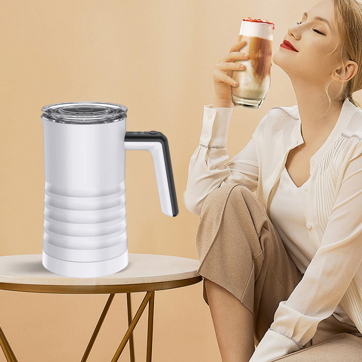Eine Frau hält einen Latte. Auf einem Tisch steht ein weißer Milchaufschäumer. Die Frau trägt ein weißes Hemd und eine braune Hose.