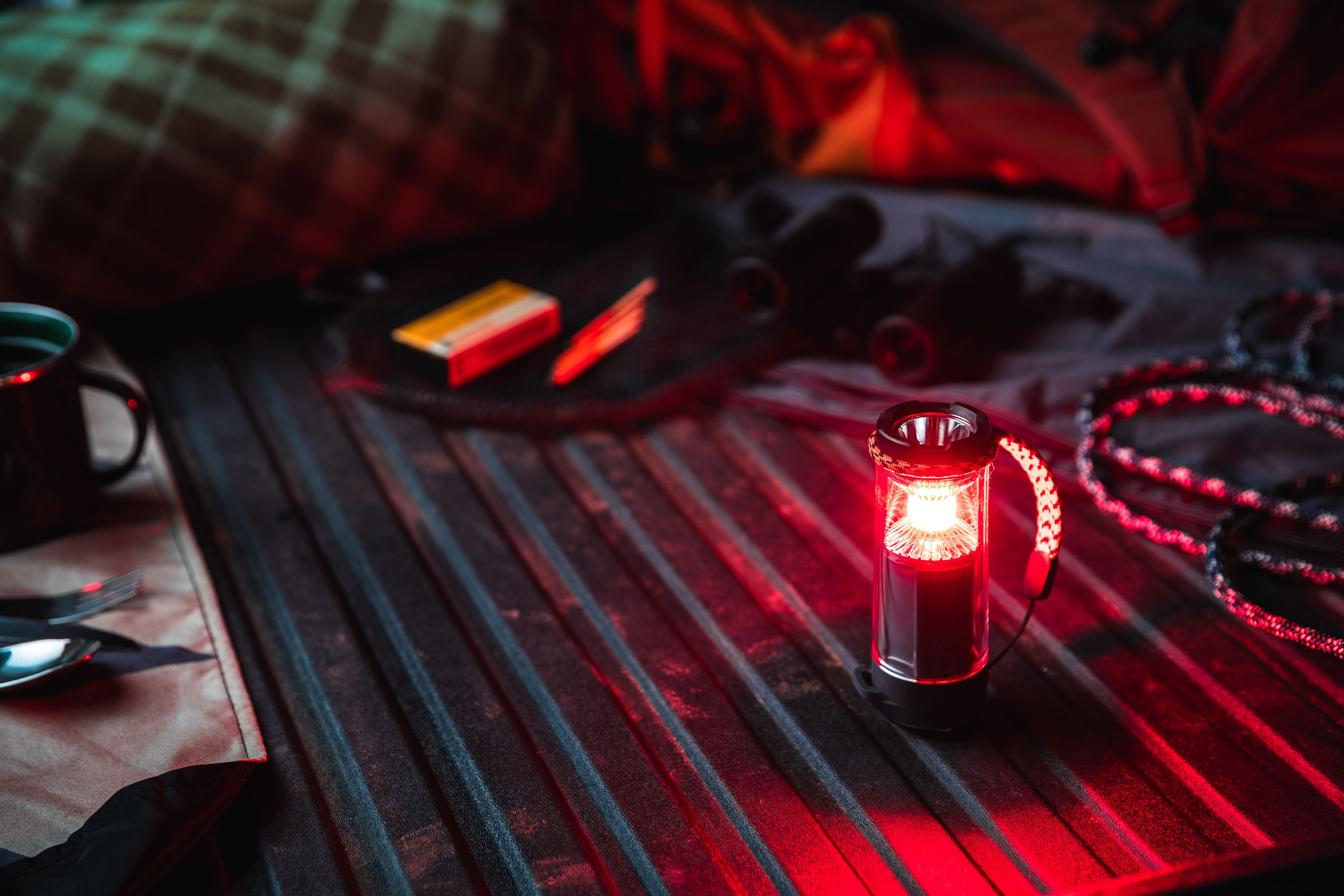 Una linterna brillante está sobre una cama de camión con equipo de campamento. También hay una taza, cubiertos, cerillas y una cuerda.