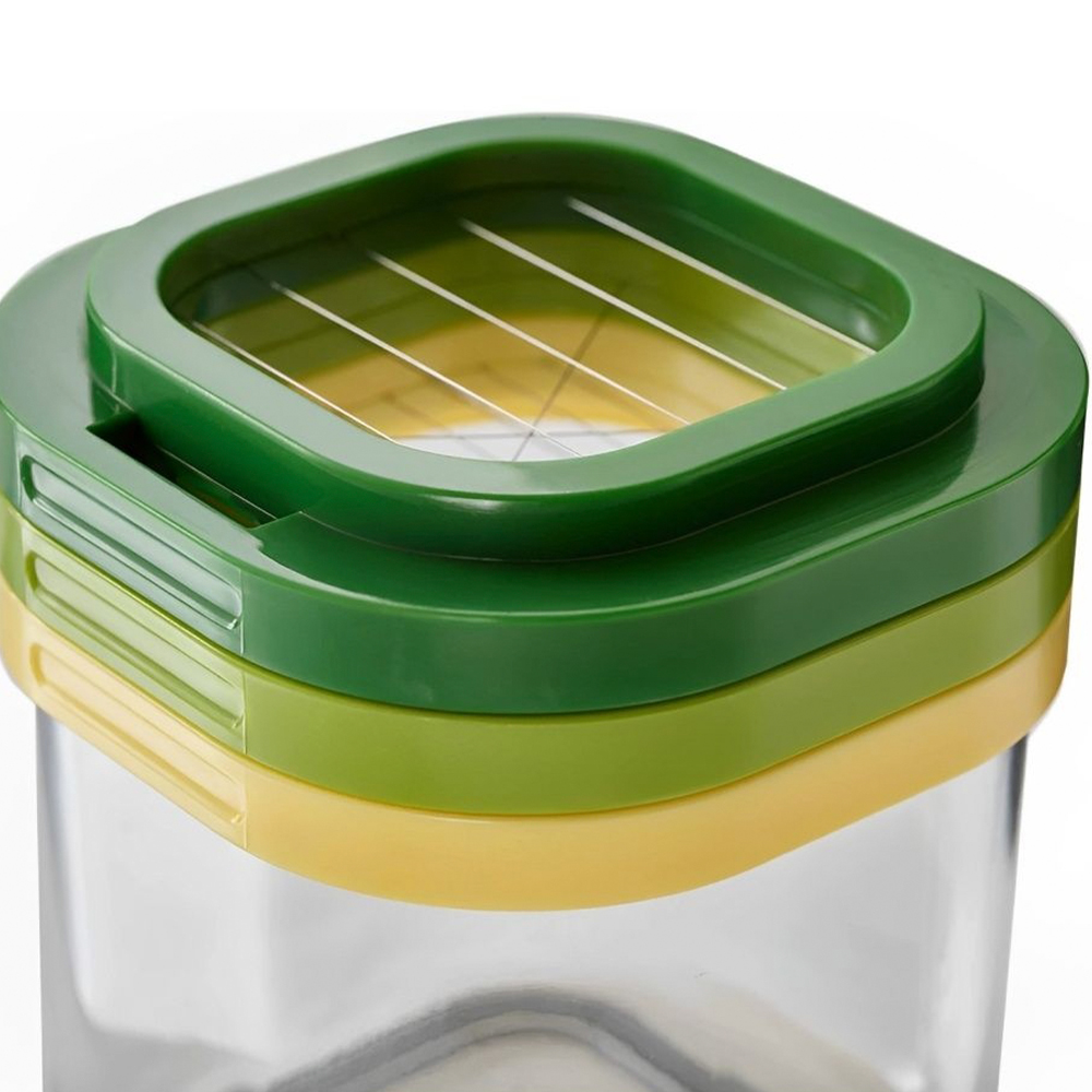 Un tritatore di verdure verde e giallo. Ha una parte superiore verde con lame, uno strato giallo e un contenitore trasparente. Sfondo bianco.