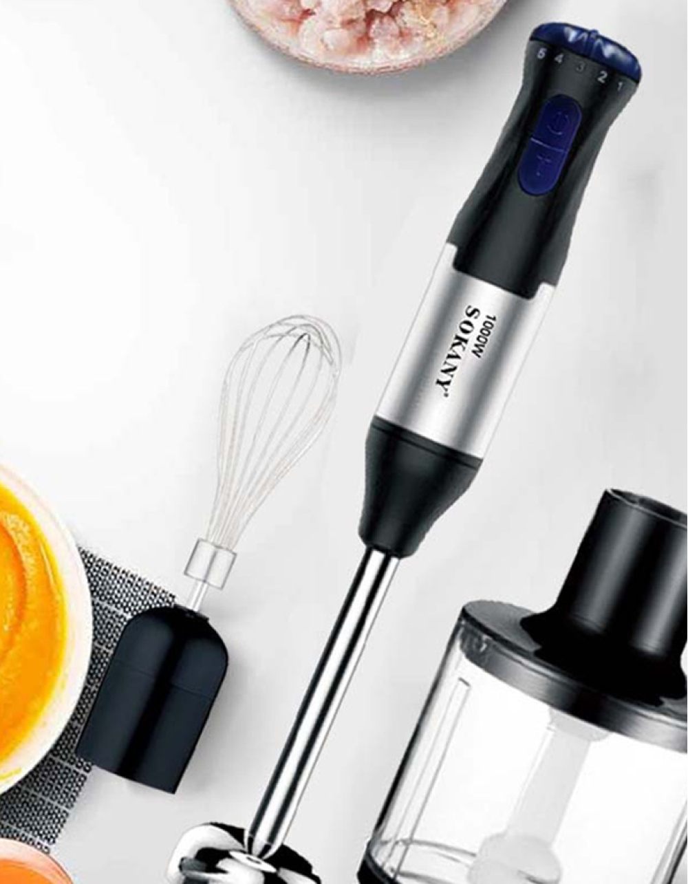 Draufsicht zeigt einen Mixer und Aufsätze auf weißer Oberfläche. Der Mixer ist schwarz und silber, mit einem Schneebesenaufsatz.
