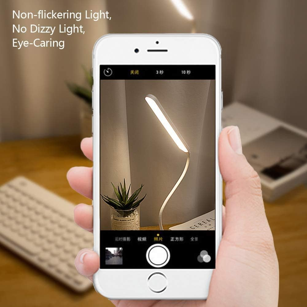 Eine Hand hält ein Telefon mit einer Schreibtischlampe. Eine kleine Pflanze und das Wort 'Cereal' sind im Hintergrund zu sehen.