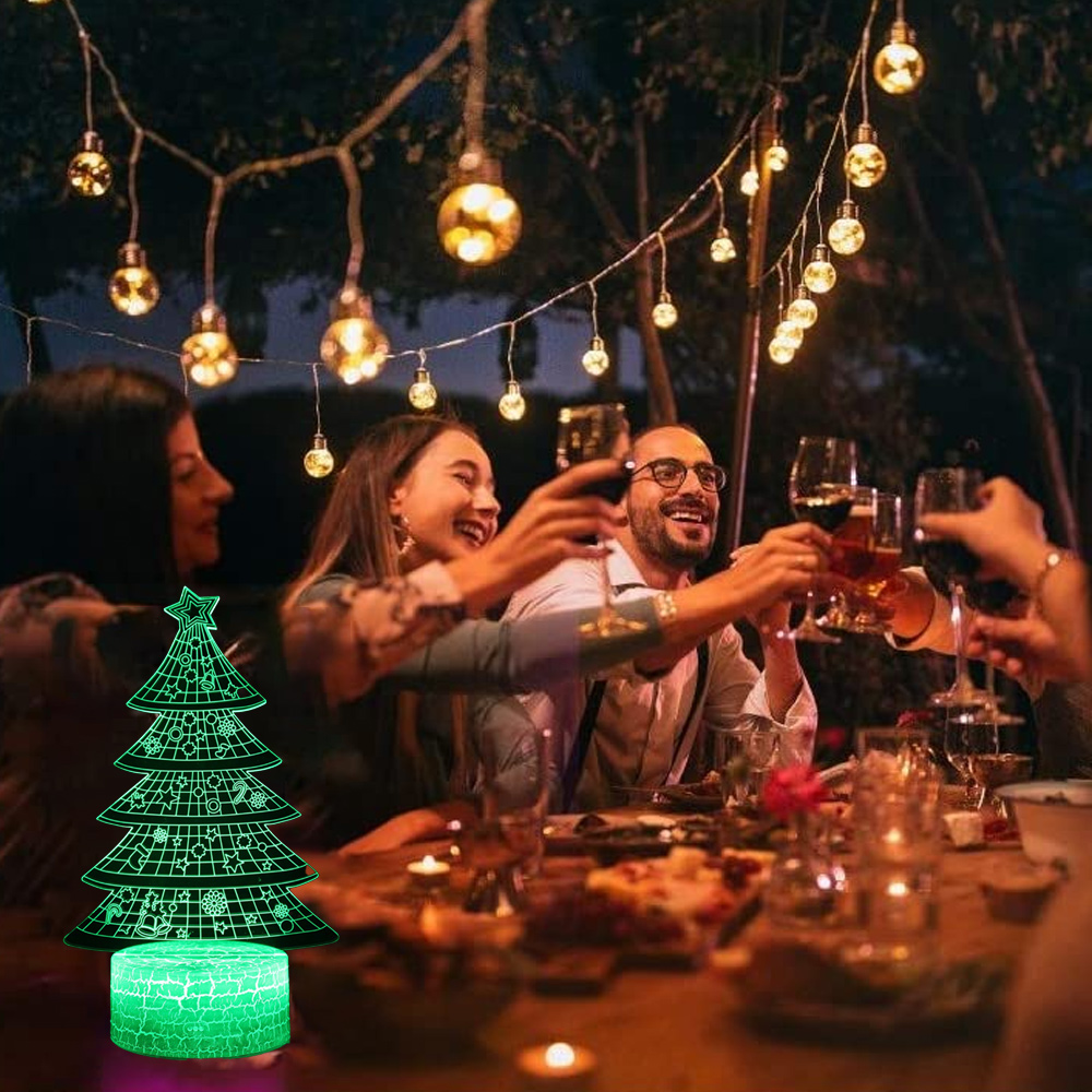 Menschen stoßen bei einer Dinnerparty mit Weingläsern an. Ein leuchtender Weihnachtsbaum steht auf dem Tisch. Lichter hängen oben.