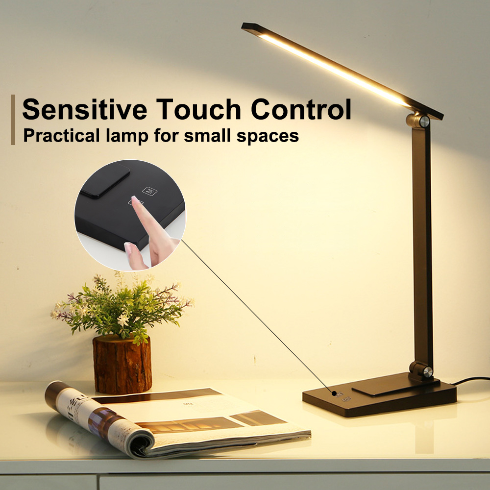 Eine moderne schwarze Schreibtischlampe leuchtet, daneben eine Zeitschrift und eine Pflanze. Ein Finger berührt die Touch-Steuerung der Lampe.