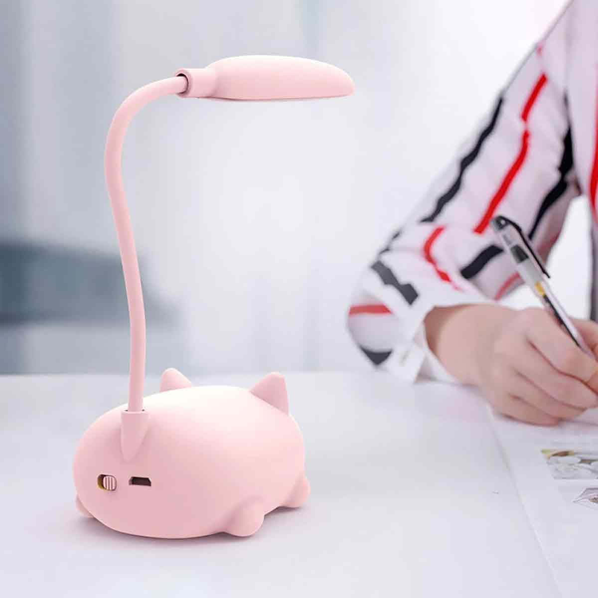 Eine rosa Schreibtischlampe in Tierform steht auf einem Schreibtisch. Eine Person in einem gestreiften Hemd schreibt mit einem Stift.