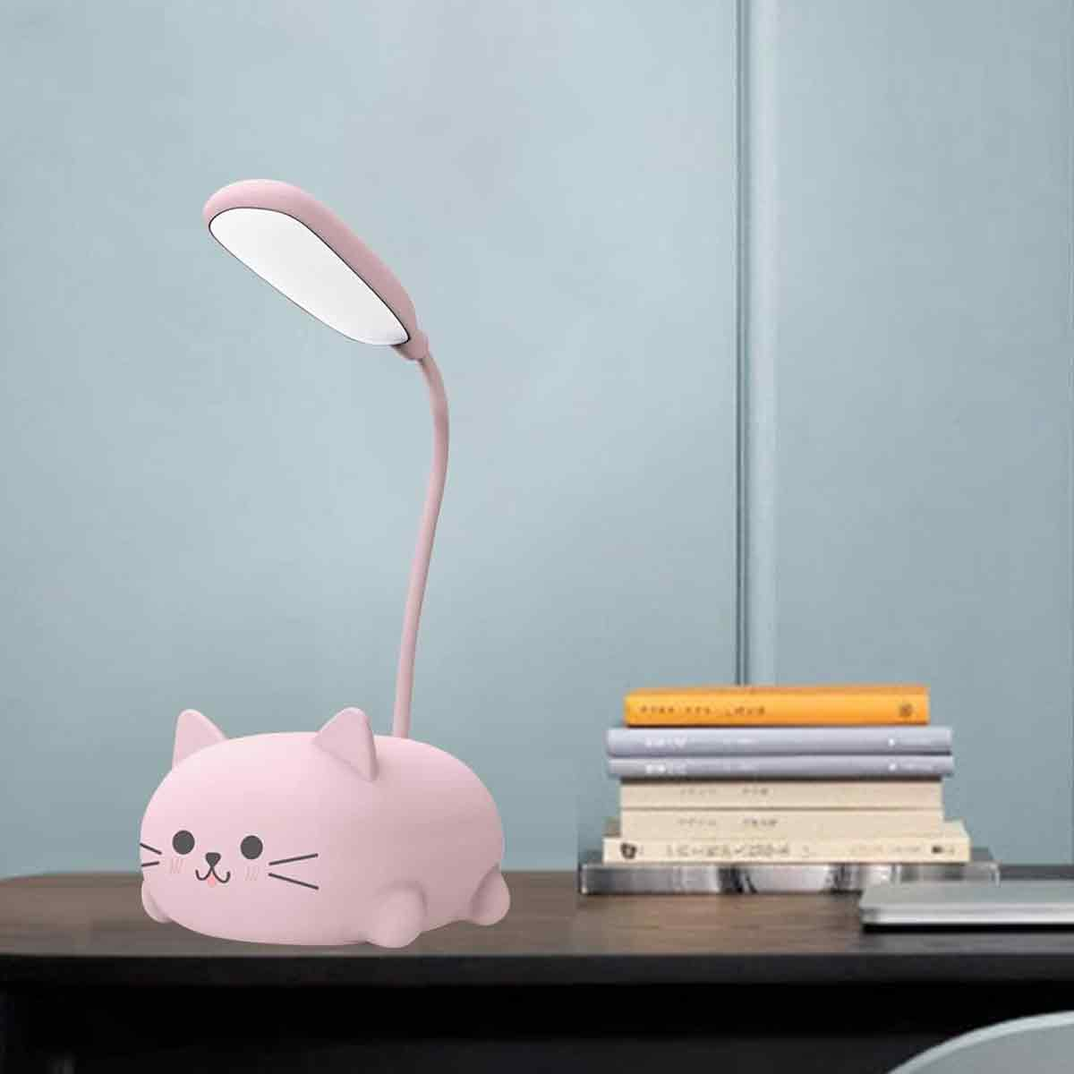 Eine rosa katzenförmige Schreibtischlampe mit flexiblem Hals und hellem Licht. Bücher sind rechts auf einer Holzoberfläche gestapelt.