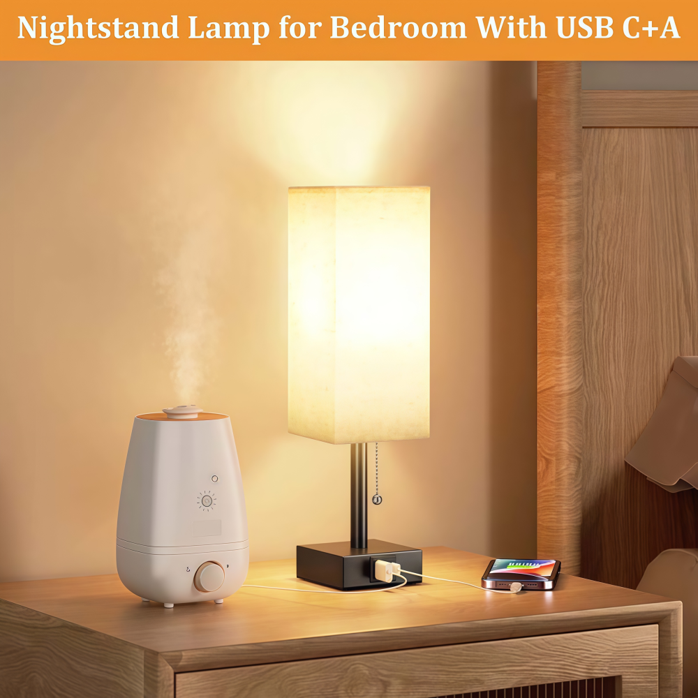 Ein Nachttisch mit Lampe, Luftbefeuchter und einem ladenden Telefon. Die Lampe ist an, der Luftbefeuchter gibt Dampf ab.