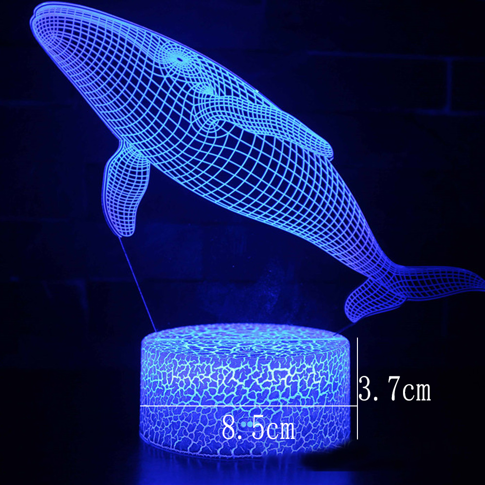 Eine blaue 3D-Wal-Lampe leuchtet. Der Wal besteht aus einem Drahtgitter-Design über einer Basis mit Rissmuster, mit Größenangaben.