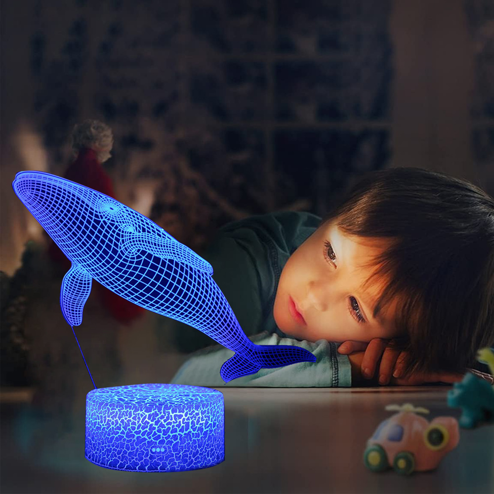 Ein Kind betrachtet eine blaue Wal-Lampe. Die Lampe leuchtet und wirft Licht auf das Kind. Spielzeug ist im verschwommenen Hintergrund.