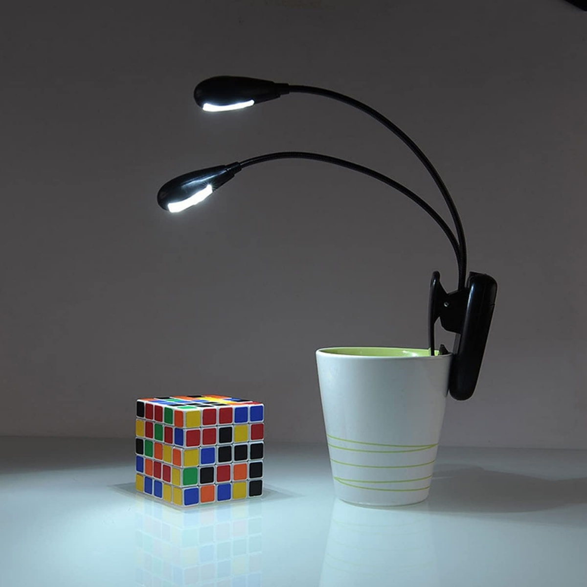 Ein Zauberwürfel steht neben einer weißen Tasse mit einer Clip-On-Lampe. Die Lampe hat zwei nach unten gerichtete Lichter.