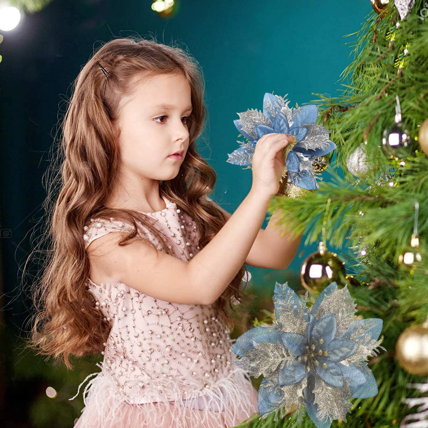Ein Mädchen schmückt einen Weihnachtsbaum mit einer blau-silbernen Poinsettie. Sie trägt ein rosa Kleid.