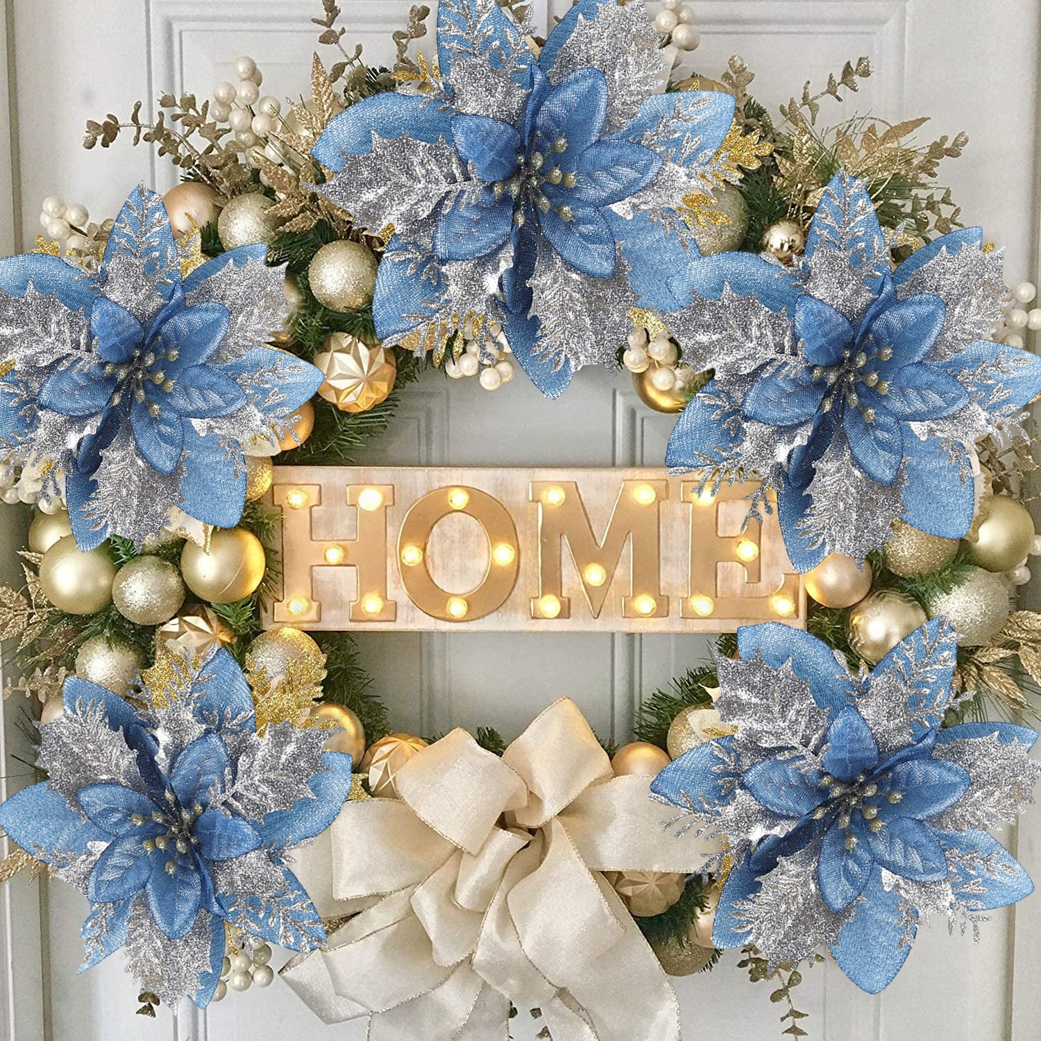 Ein dekorativer Kranz mit blauen und silbernen Poinsettien, goldenen Ornamenten und einer cremefarbenen Schleife mit dem Schriftzug 'HOME'.