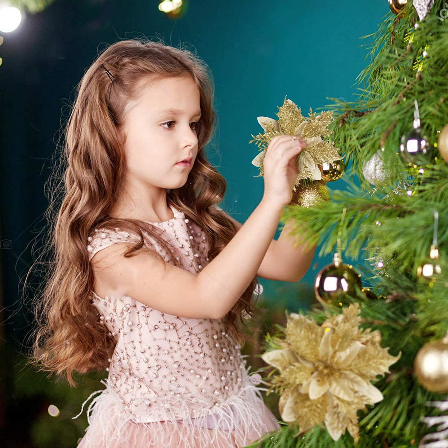 Ein Mädchen schmückt einen Weihnachtsbaum mit goldenen Ornamenten und Blumen. Sie trägt ein rosa Kleid.