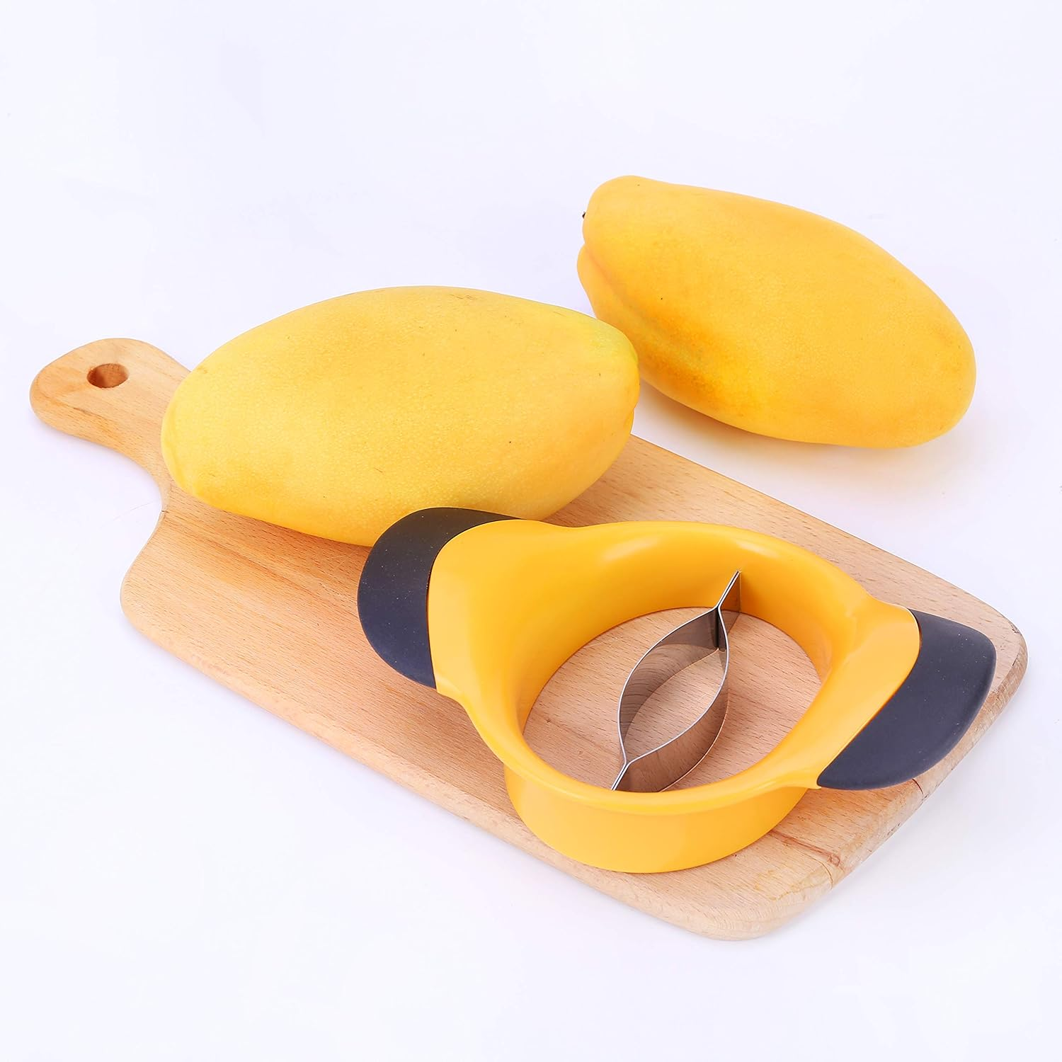 Drei gelbe Mangos, ein Mangoschneider und ein Holzschneidebrett auf einer weißen Oberfläche. Der Schneider ist gelb und schwarz.