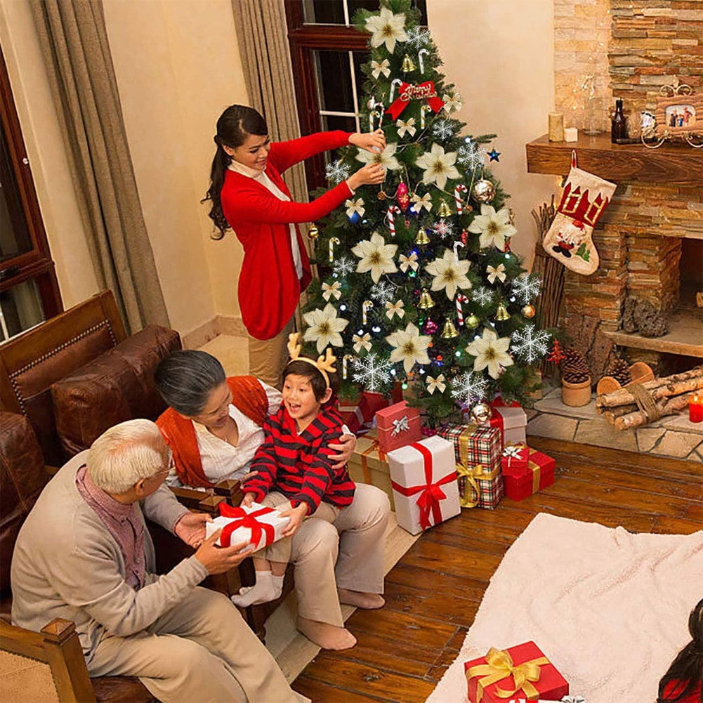 Familie schmückt Weihnachtsbaum. Eine Frau in Rot hängt Ornamente auf, während andere Geschenke öffnen. Ein Kamin ist sichtbar.