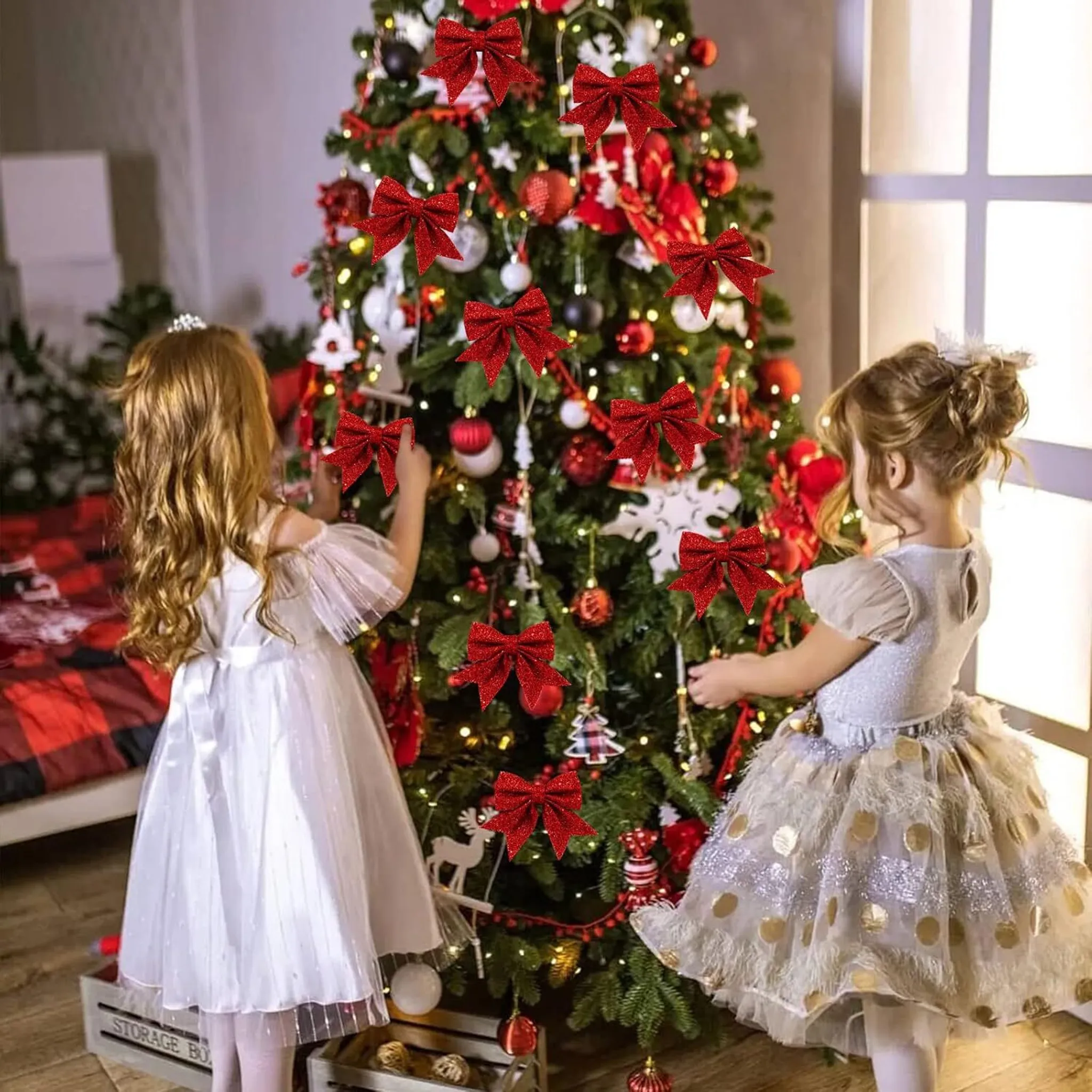 Zwei Mädchen schmücken einen Weihnachtsbaum mit roten Schleifen. Der Baum ist mit Lichtern und Ornamenten geschmückt. Die Mädchen tragen Kleider.
