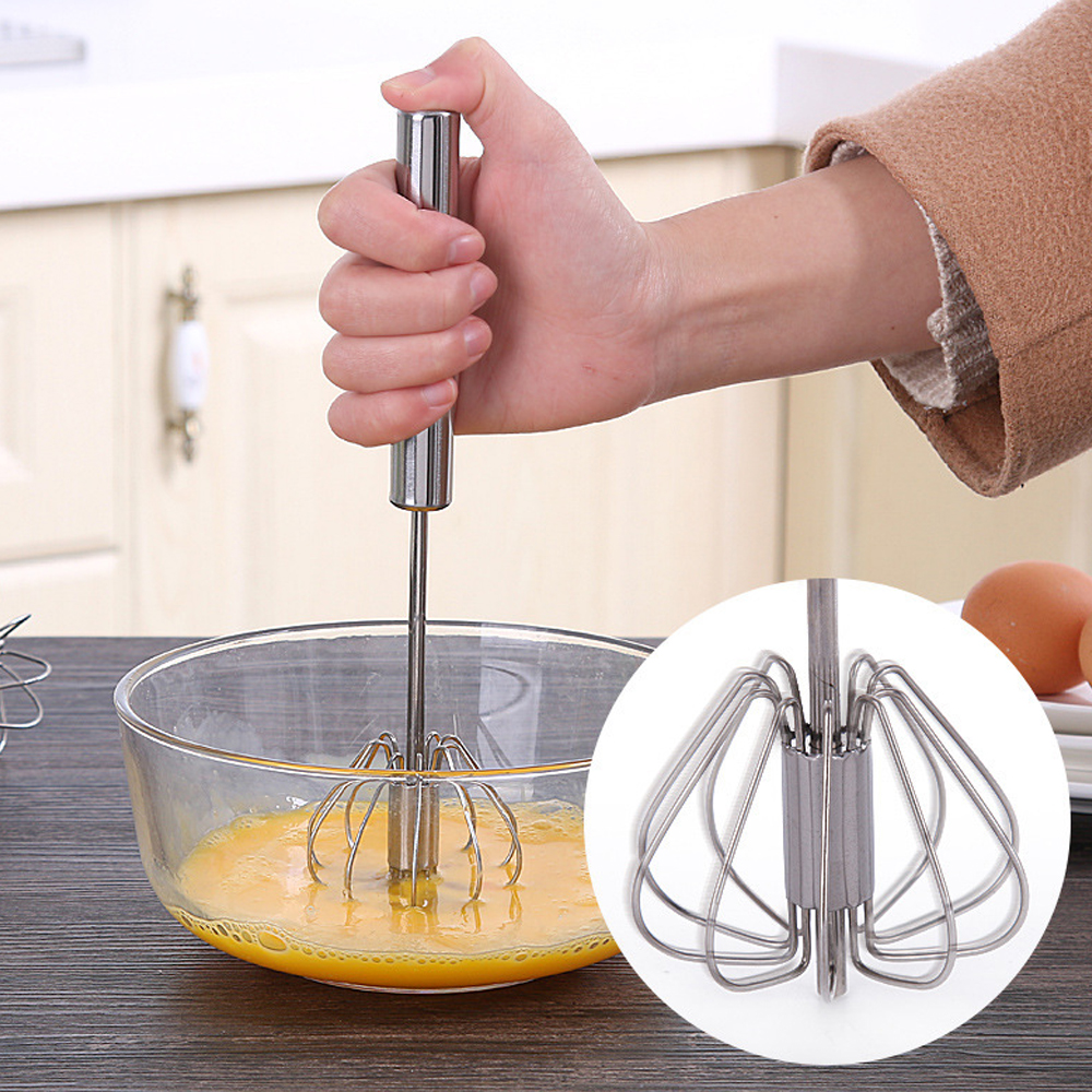 Eine Hand hält einen Schneebesen über einer Schüssel mit gelber Flüssigkeit. Nahaufnahme des Drahtes. Eier im Hintergrund.