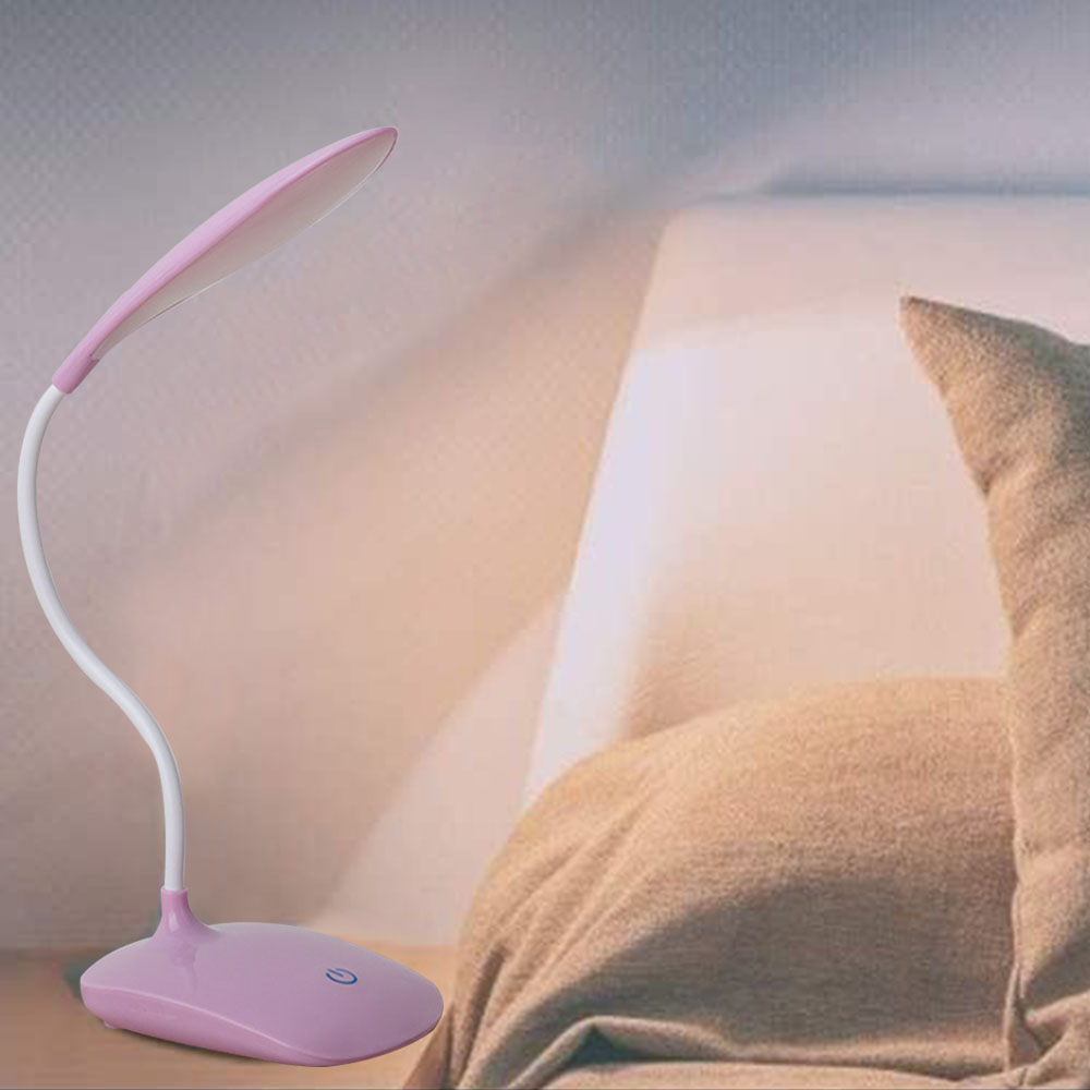 Eine rosa Schreibtischlampe mit gebogenem Hals und weißem Sockel steht neben einem Bett mit beigem Kissen.