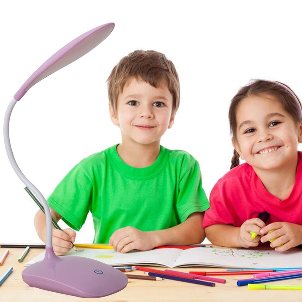 Zwei lächelnde Kinder mit einer Schreibtischlampe. Der Junge trägt Grün, das Mädchen Rosa. Buntstifte liegen auf dem Tisch.