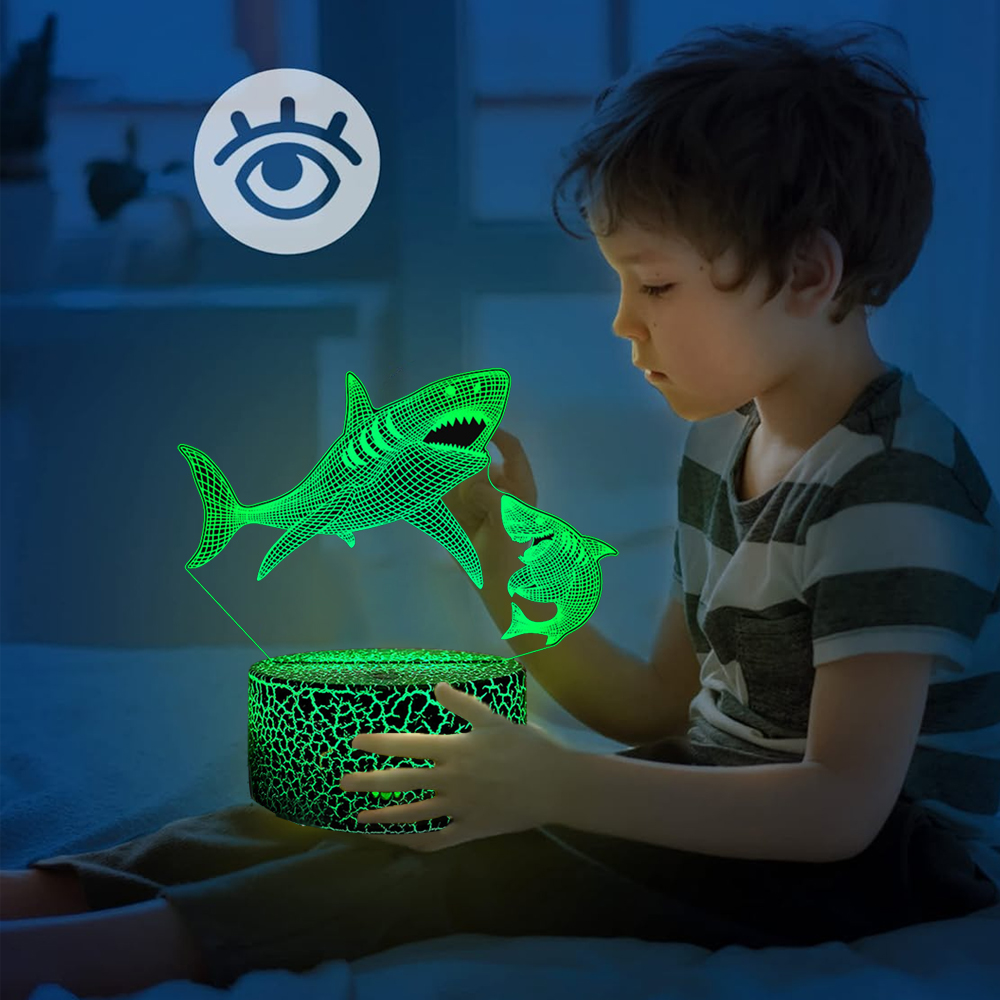 Ein Junge betrachtet eine grüne Hai-Lampe. Die Lampe steht auf einem Tisch. Der Hintergrund ist eine blaue Wand.