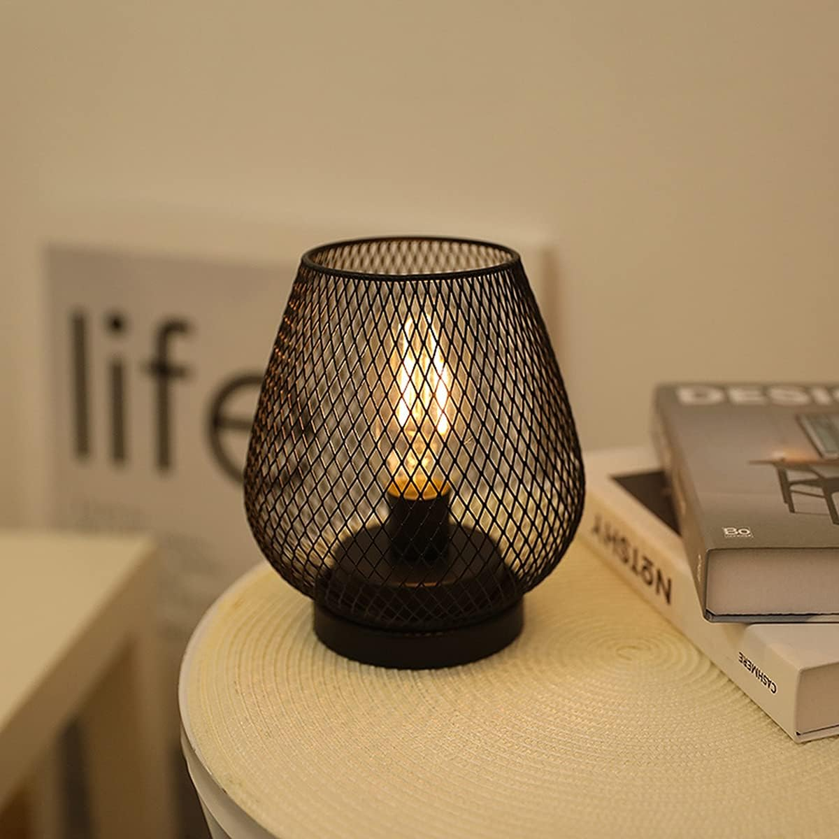 Eine beleuchtete schwarze Metalllampe mit Rautenmuster steht auf einem Tisch. Bücher und das Wort 'Leben' sind im Hintergrund.