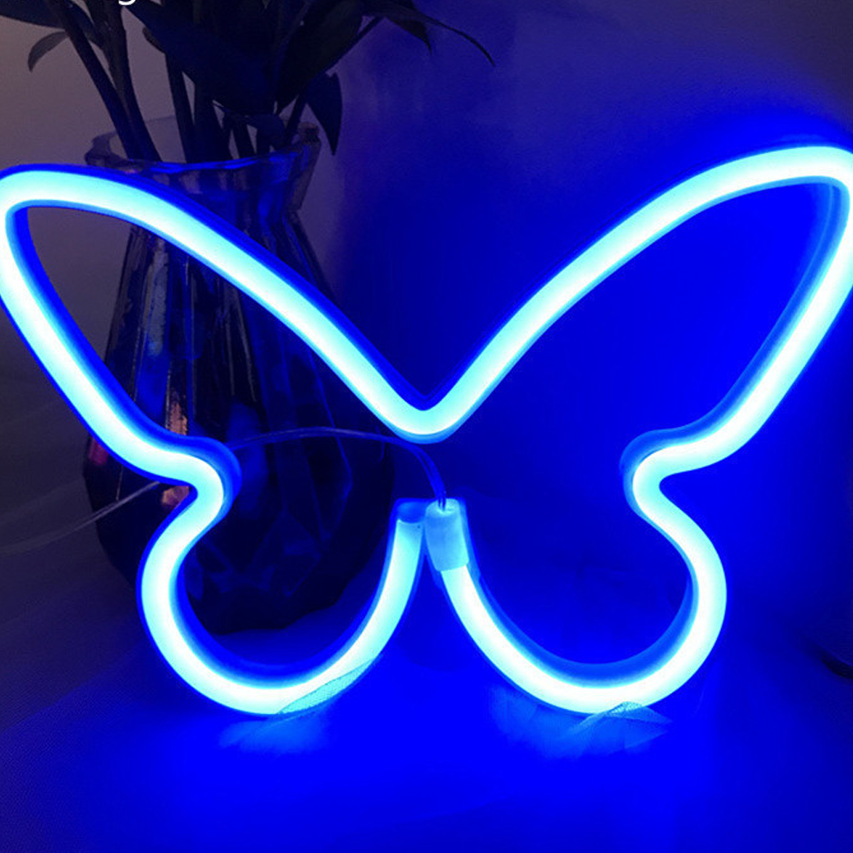Ein blaues Neon-Schmetterlingslicht ist eingeschaltet. Im Hintergrund befindet sich eine Vase mit Pflanzen. Die Szene wird von dem Neonlicht beleuchtet.