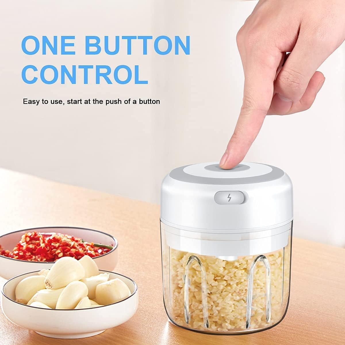 Eine Hand drückt einen Knopf auf einem weißen Food-Processor. Schalen mit Knoblauch und gehackten roten Paprika sind im Vordergrund.