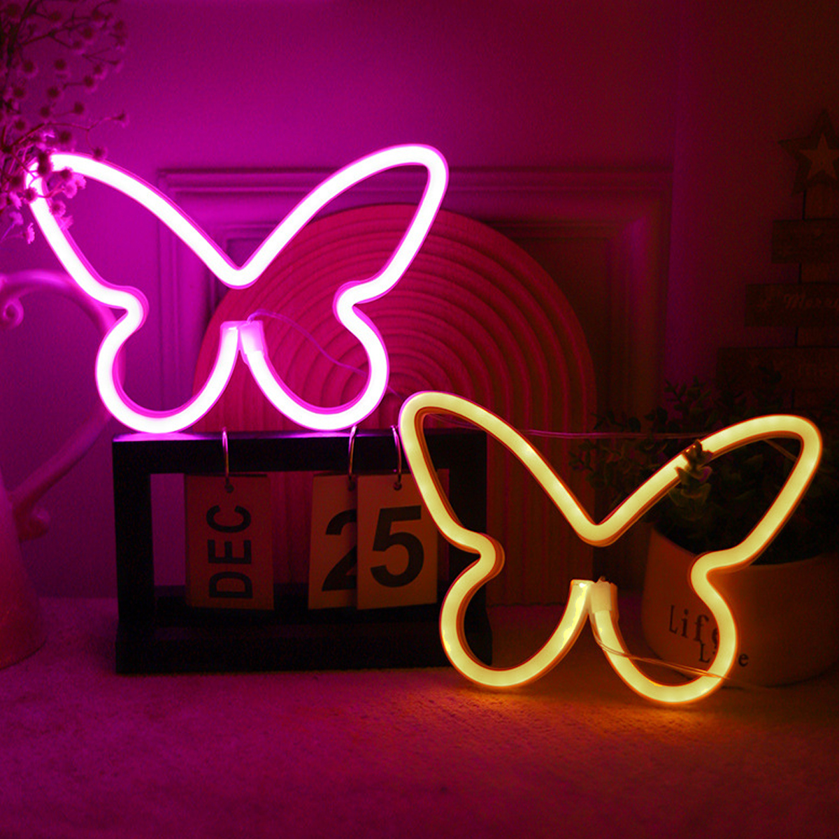 Zwei Neon-Schmetterlingslichter, eines rosa, eines gelb, auf einem Tisch mit einem Kalender, der den 25. Dezember zeigt.