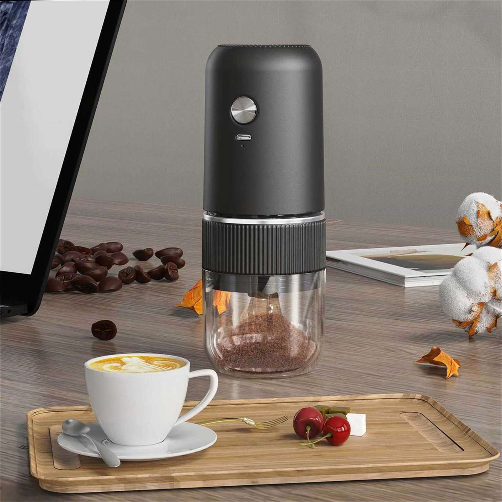 Eine Kaffeemühle und eine Tasse Kaffee auf einem Holztisch mit Kaffeebohnen und Kirschen.
