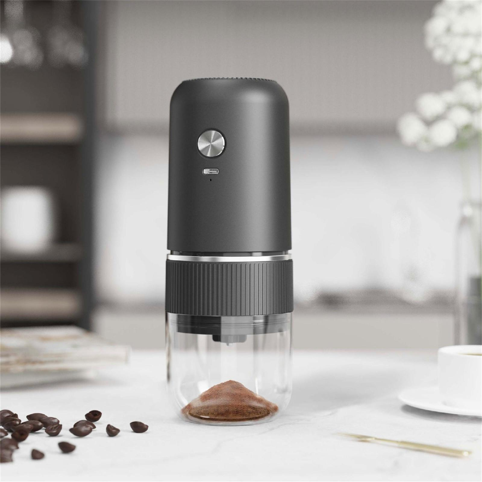 Eine schwarze Kaffeemühle mit gemahlenem Kaffee. Kaffeebohnen sind auf der weißen Oberfläche verstreut.