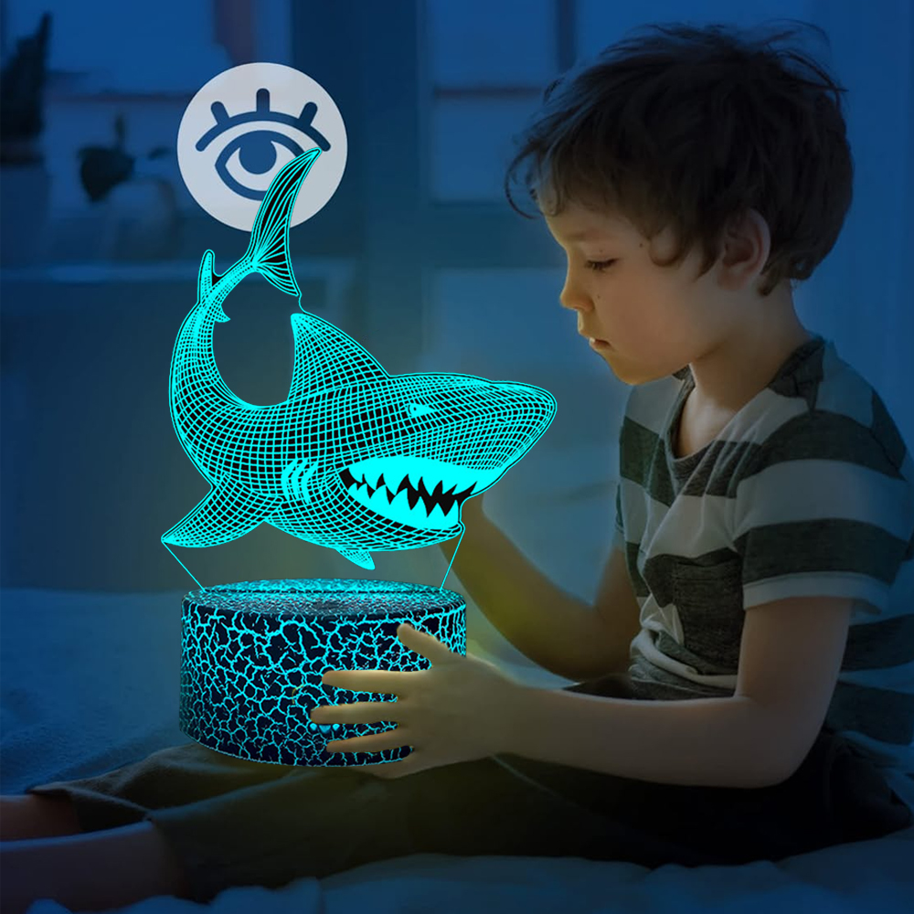 Ein Junge betrachtet eine leuchtende Hai-Lampe. Die Lampe ist blau mit einer weißen Augengrafik darüber. Der Junge trägt ein gestreiftes Hemd.