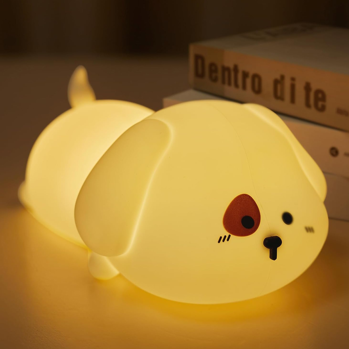 Ein leuchtendes, hundeförmiges Nachtlicht liegt auf einer Oberfläche. Im Hintergrund befindet sich ein Buch mit dem Titel 'Dentro di te'.