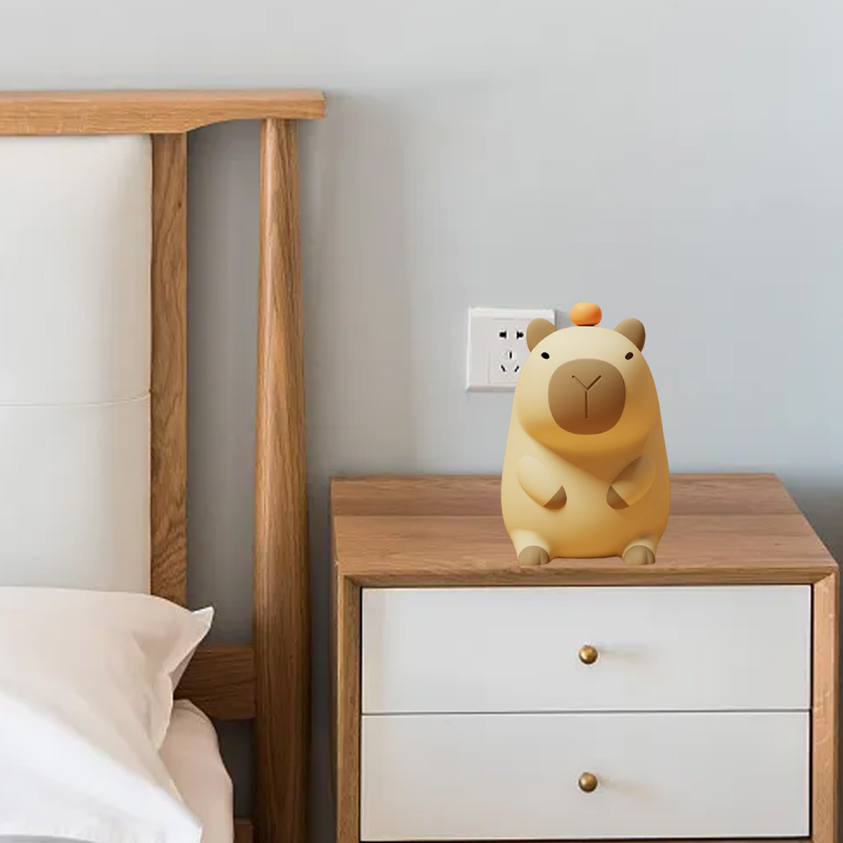 Eine Cartoon-Bärenlampe steht auf einem Nachttisch aus Holz. Der Hintergrund zeigt ein Bett, eine Steckdose und eine hellblaue Wand.