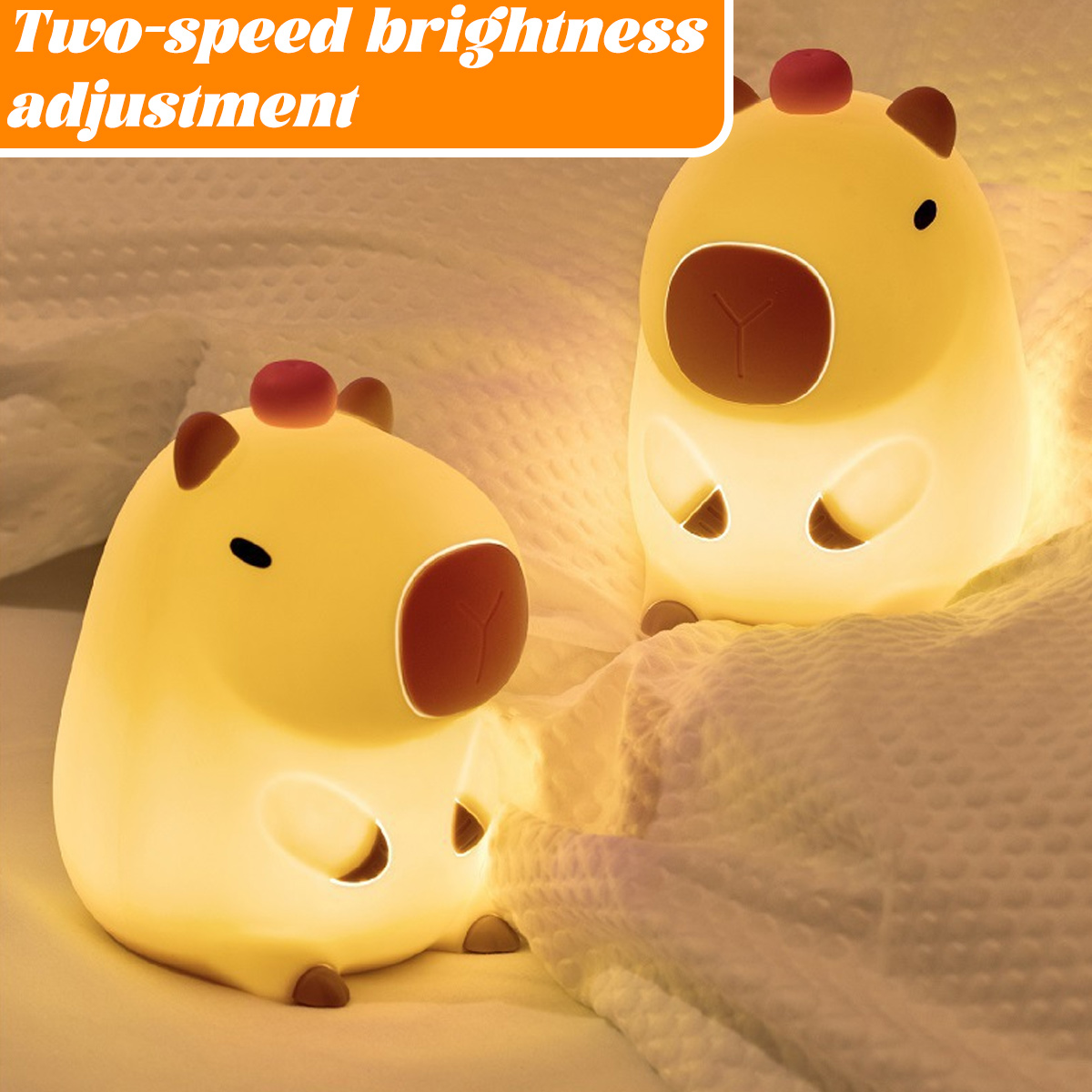 Zwei leuchtende Capybara-Nachtlichter, gelb mit braunen Details, liegen auf einem Bett. Die Lichter beleuchten die Bettwäsche.