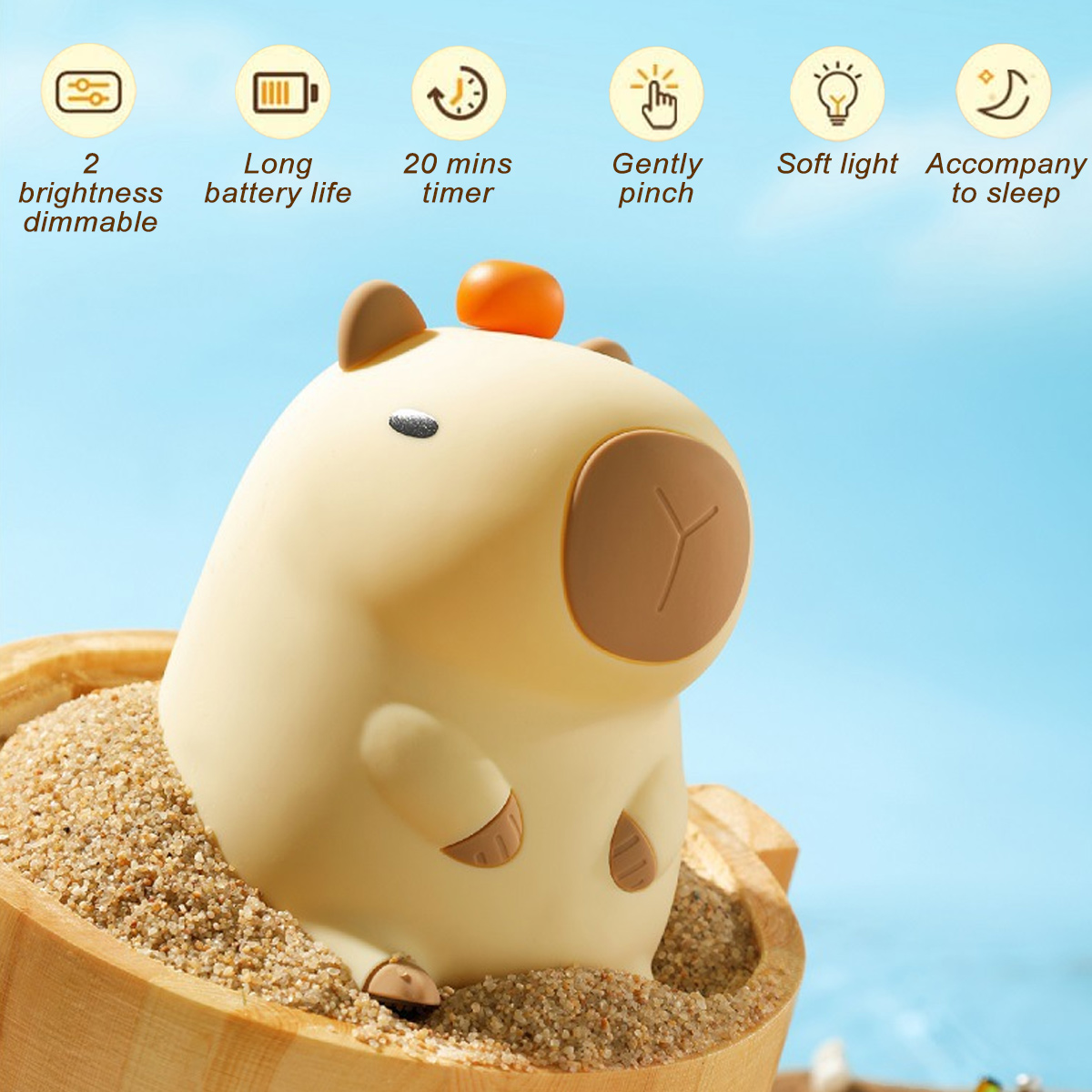 Ein nachtlichtförmiges, beiges Capybara sitzt in einem Holzbehälter mit Sand. Es hat braune Details und eine orangefarbene Oberseite. Der Hintergrund ist blau.