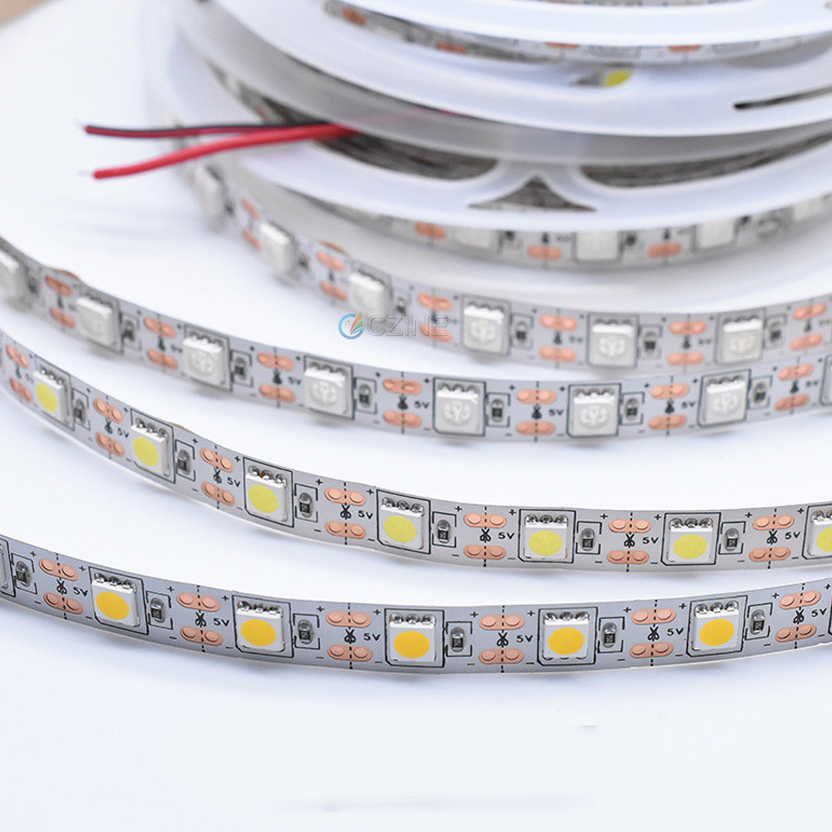 Nahaufnahme von LED-Lichtleisten auf weißer Oberfläche. Die Lichter sind auf einer Rolle, rote und schwarze Drähte sichtbar. Details umfassen Widerstände.