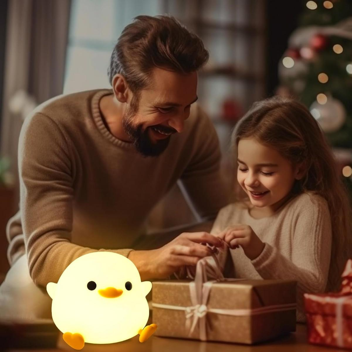 Ein Mann und ein Mädchen öffnen ein Geschenk. Vorne steht eine leuchtende Kükenlampe. Weihnachtsbaum im Hintergrund.
