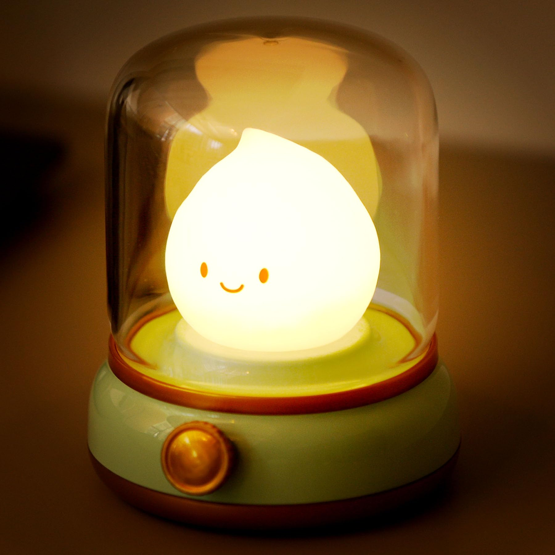 Ein niedliches Nachtlicht mit einem lächelnden Gesicht in einer Glaskuppel. Es hat einen grünen Sockel und einen goldenen Knopf.