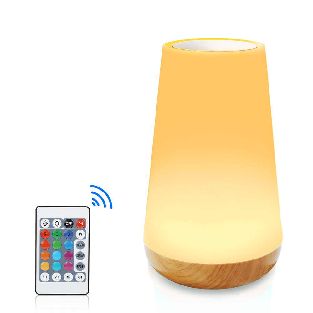 Eine leuchtende Lampe mit Holzsockel und Fernbedienung. Die Lampe strahlt ein weiches, warmes Licht aus. Die Fernbedienung hat Farbtasten.