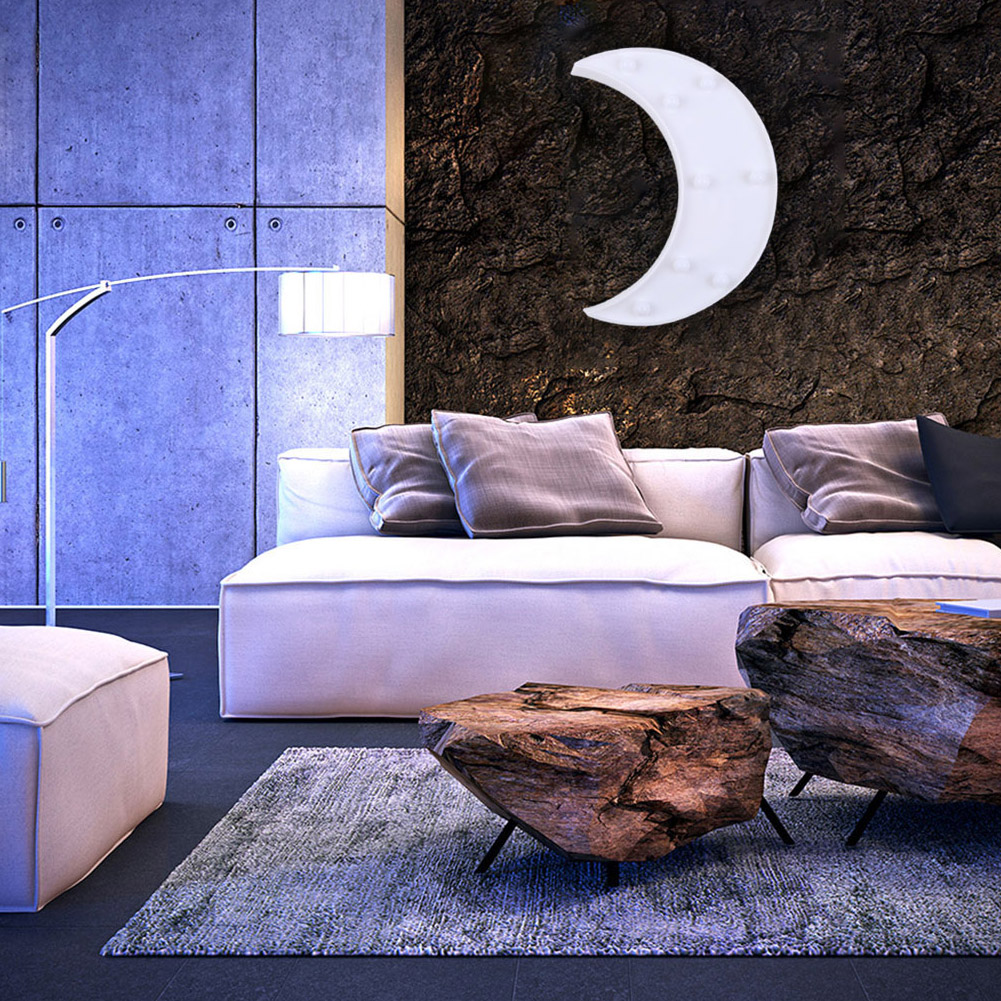 Wohnzimmer mit weißem Sofa, Steintischen und mondförmigem Licht an einer strukturierten Wand. Eine Lampe und eine Ottomane sind vorhanden.