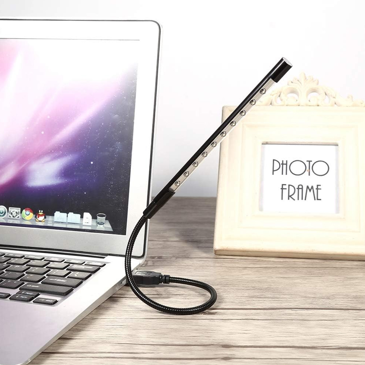 Un laptop con una luce LED USB collegata. Una cornice è dietro il laptop su una superficie di legno.