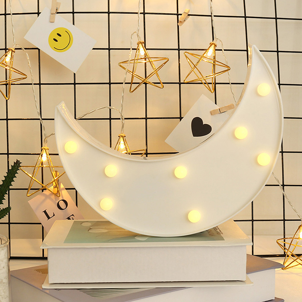 Eine weiße mondförmige Lampe mit Lichtern auf Büchern. Sternlichter hängen an einem Gitter. Karten mit einem Smiley und einem Herzen sind befestigt.
