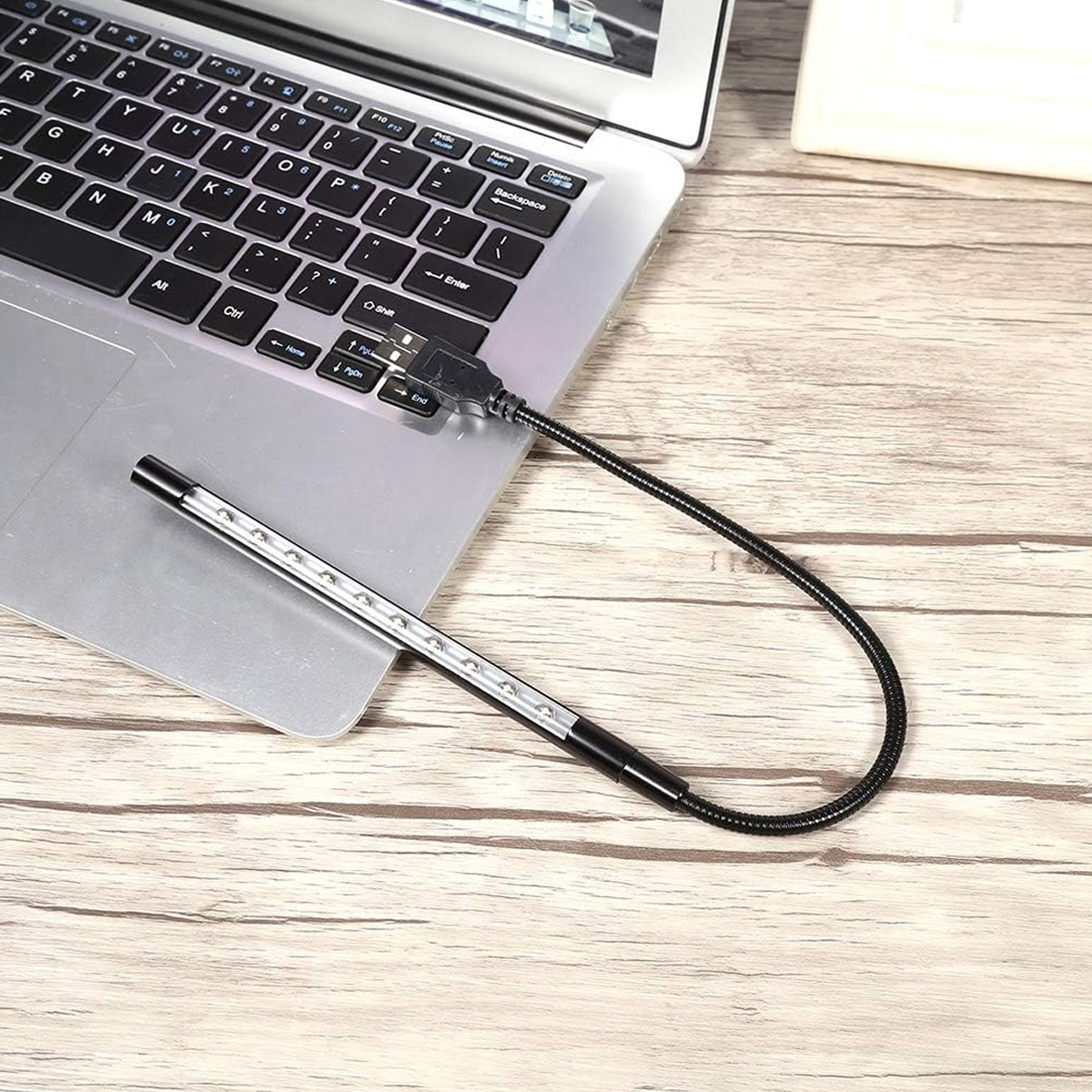 Un laptop con una luce USB collegata su una superficie di legno. La luce è flessibile e ha più luci piccole.